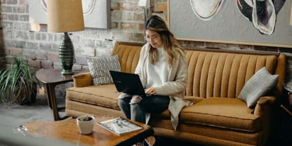 A woman sitting on a couch, using a laptop to manage a multi-channel marketing automation tool.